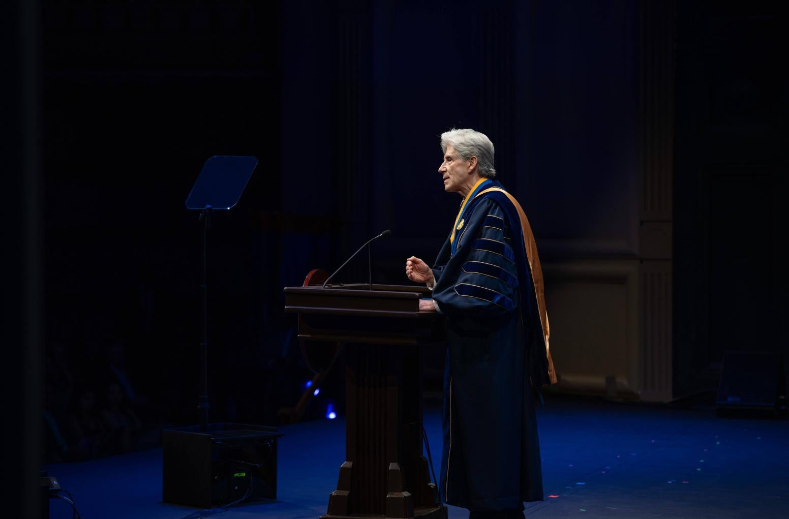 Julio Frenk, in dark blue academic robe, standing onstage at a podium
