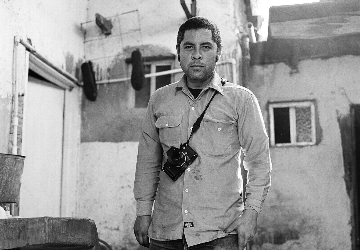 A man with a camera strapped around his chest poses in front of a prominent building