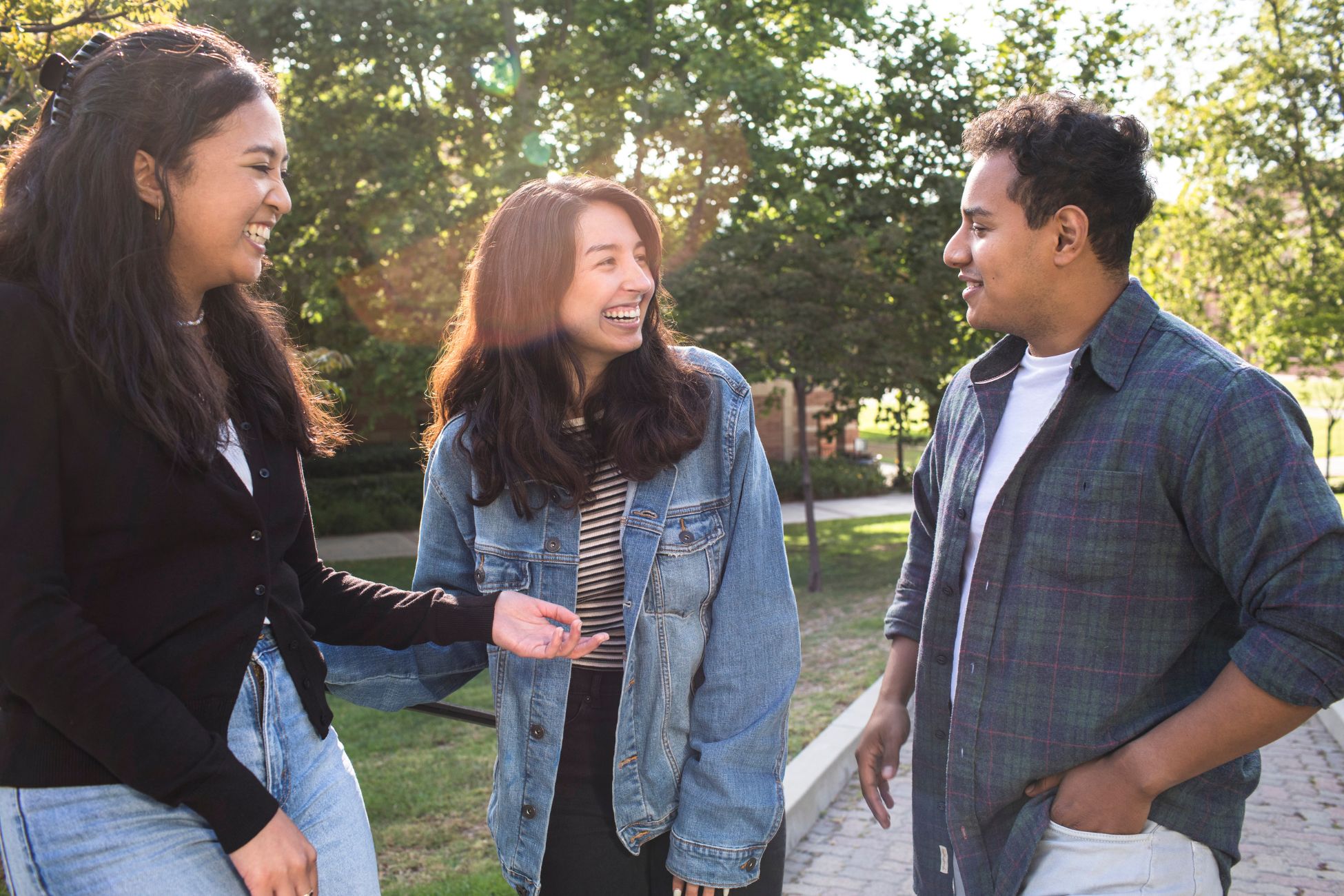 One male and two female students, all with dark hair and medium toned skin, smile and laugh together