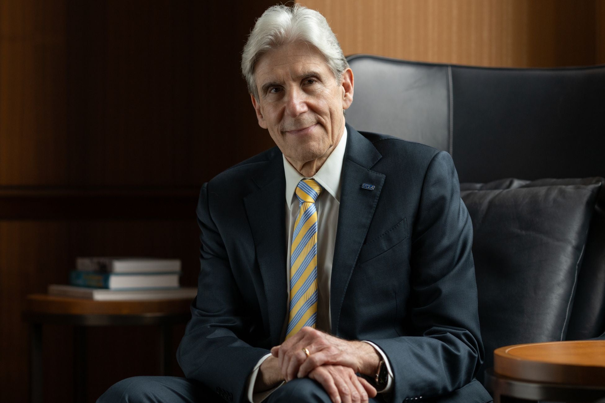 Chancellor Frenk sits in a chair wearing a suit, showcasing a polished and professional demeanor