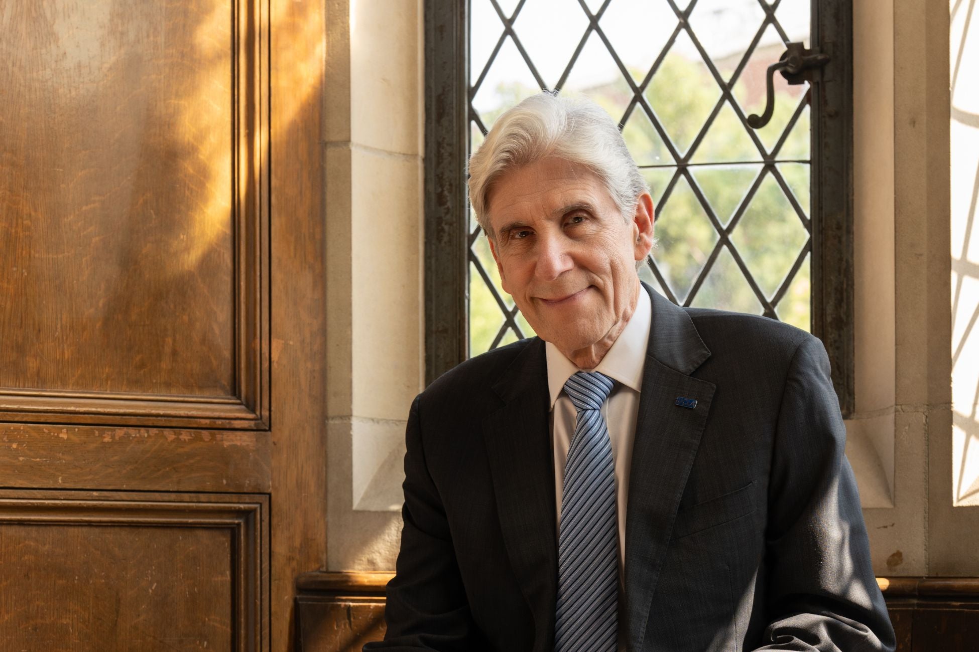 Chancellor Frenk sits by a window, smiling and wearing a suit