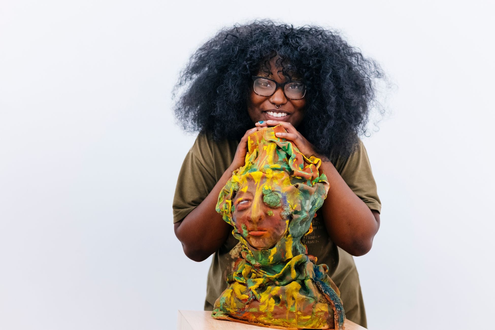 African American woman with full curly hair and glasses smiles behind a colorful ceramic sculpture