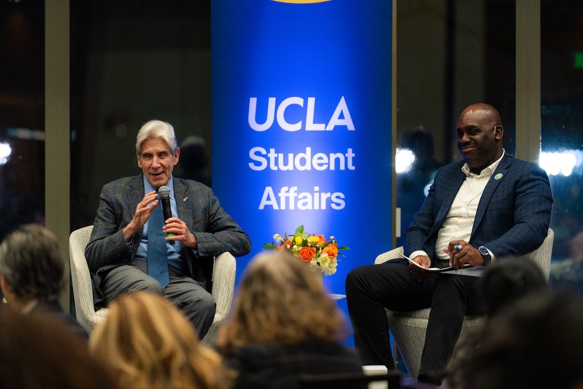 Julio Frenk, left, and Monroe Gorden Jr. sit on either side of a UCLA Student Affairs banner