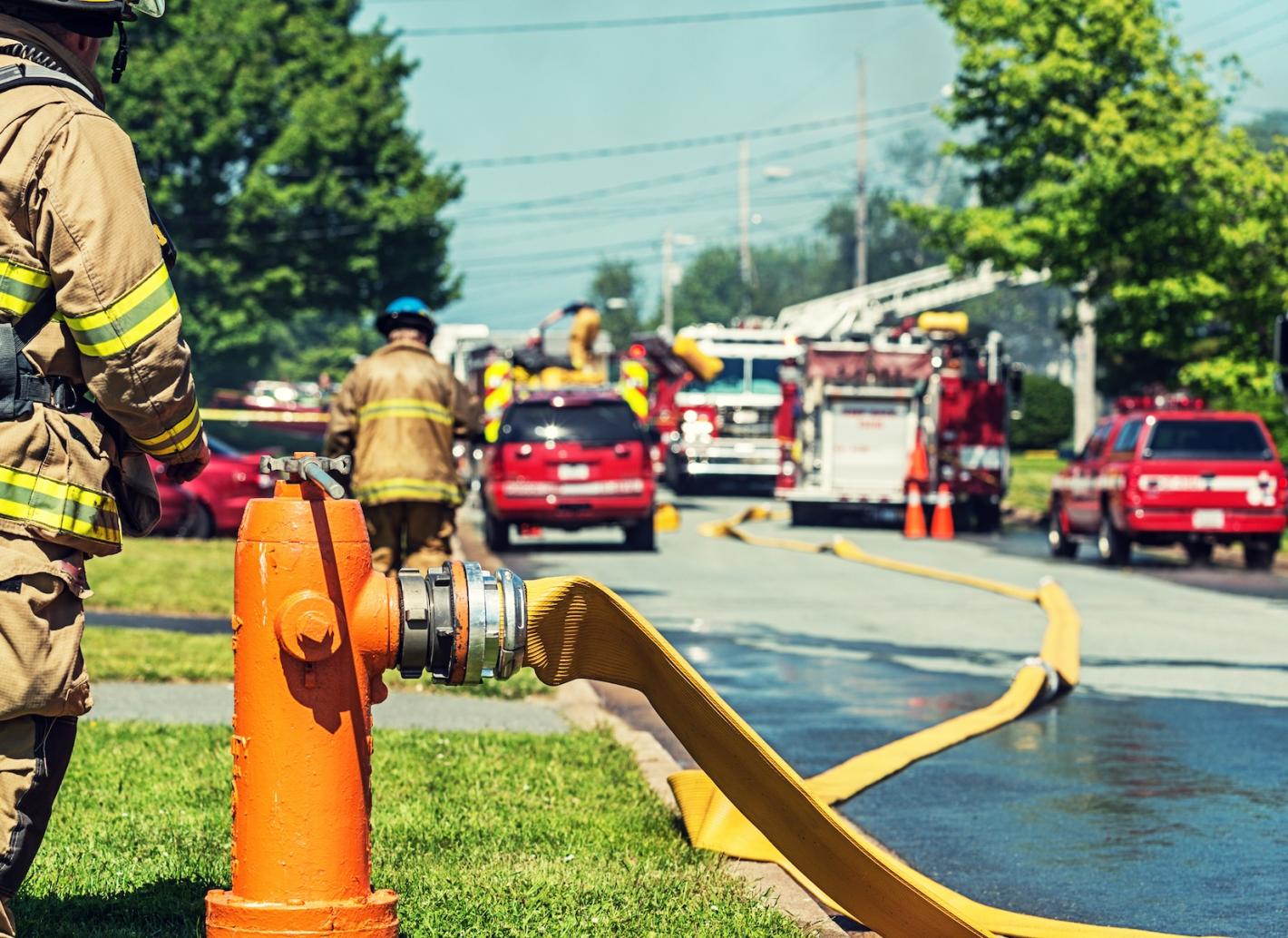 Fire hydrant in foreground, with firefighters, hoses and fire trucks in background