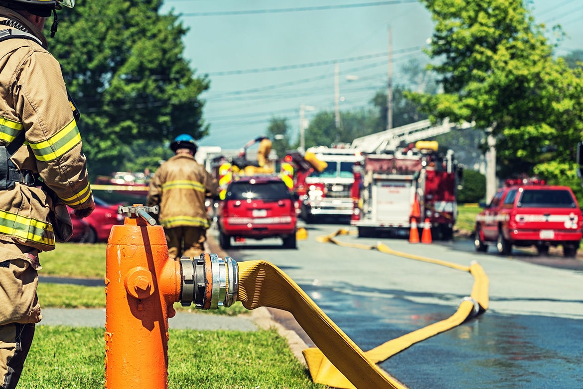 Fire hydrant in foreground, with firefighters, hoses and fire trucks in background