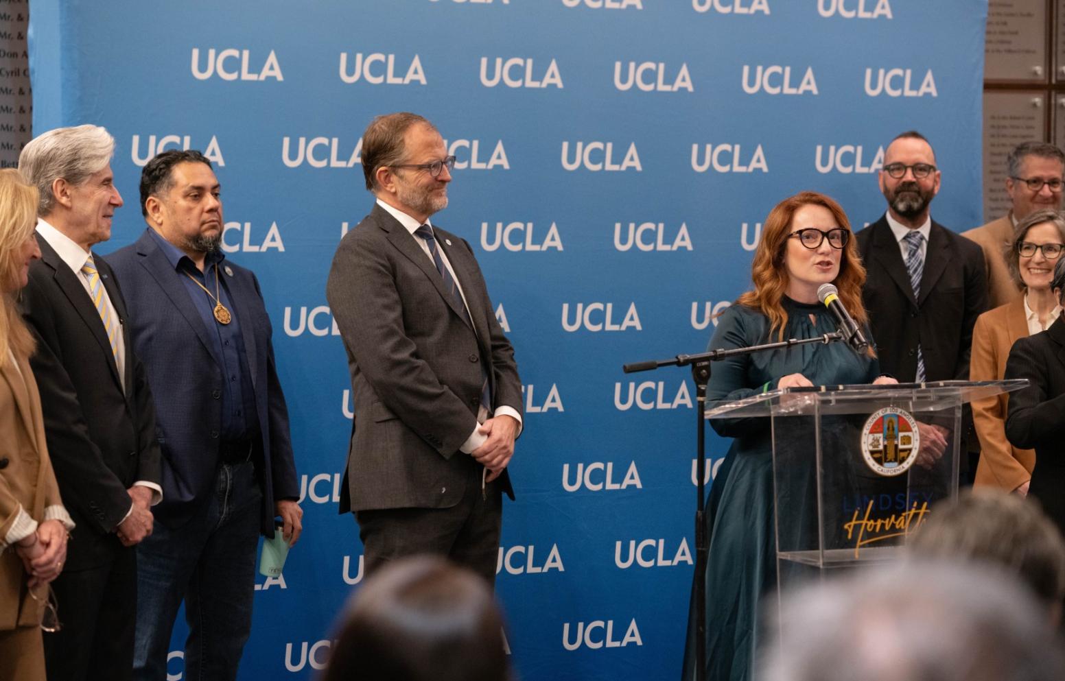 UCLA Chancellor Julio Frenk watches as County Supervisor Lindsey Horvath speaks at the podium