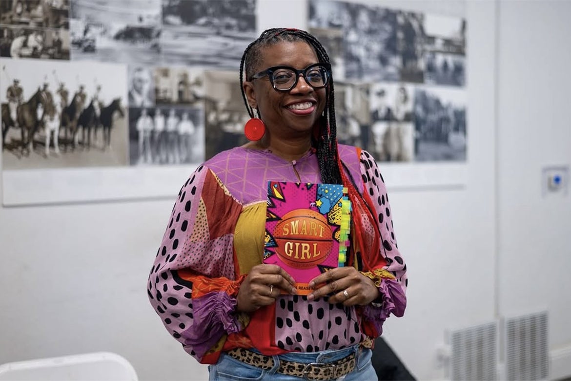 La’Tonya Rease Miles, in colorful top and black-rimmed glasses, holds a copy of her memoir, “Smart Girl: A First-Gen Origin Story”