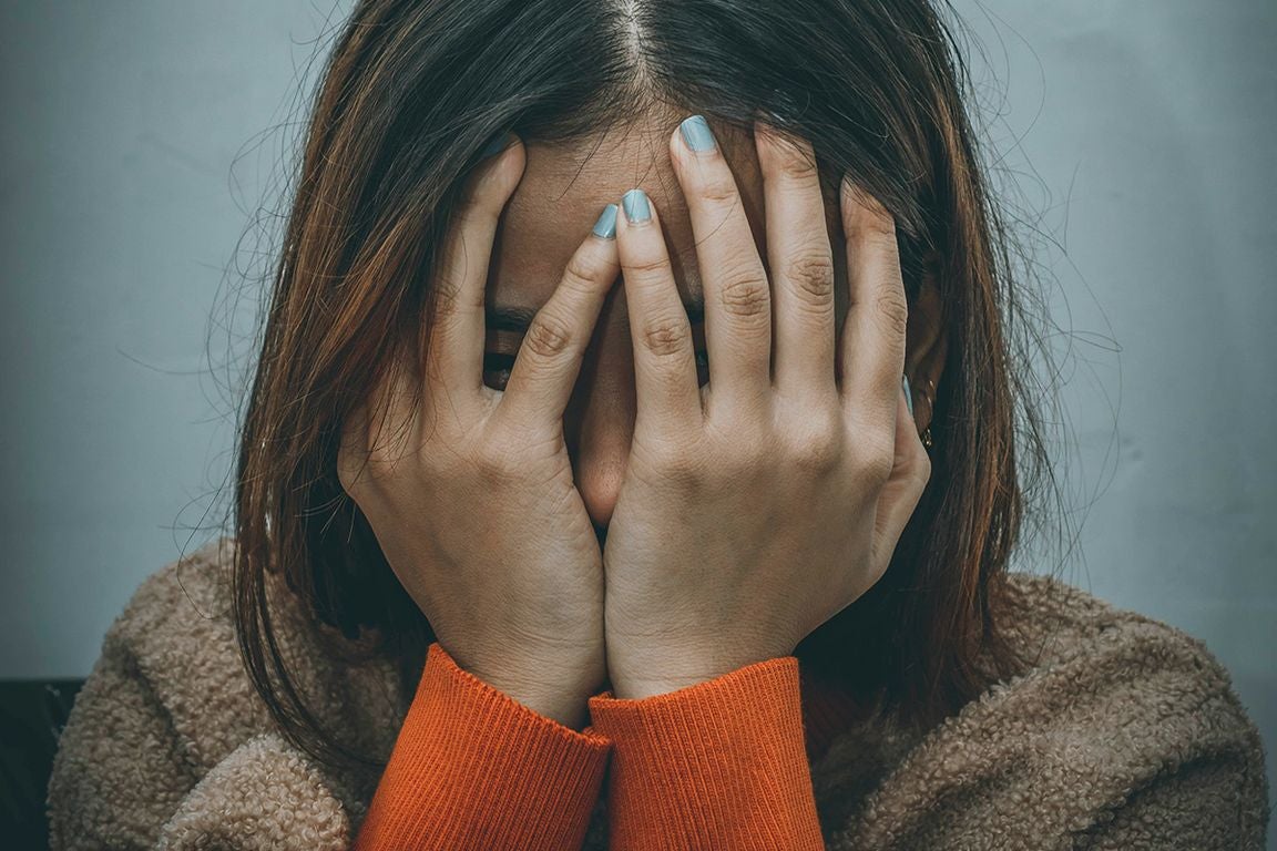 Woman in brown sweater holds her hands in front of her face