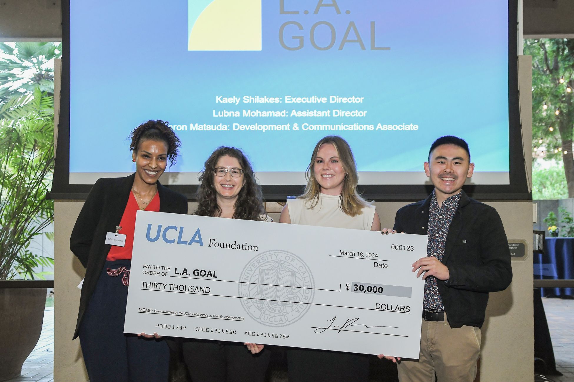Four people of varying ethnicities hold a large check and smile at the camera.