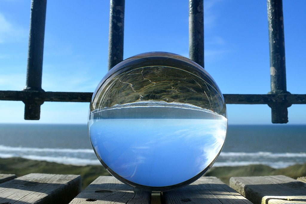 A crystal ball showing inverse sky and land; ocean in the background behind the ball