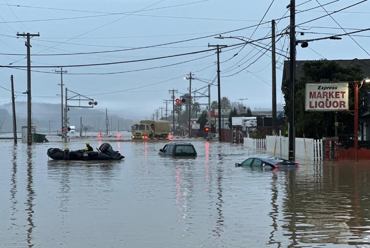 Submerged cars float in the forefront as a National Guard vehicle approaches a flooded railroad track in Monterey County, California