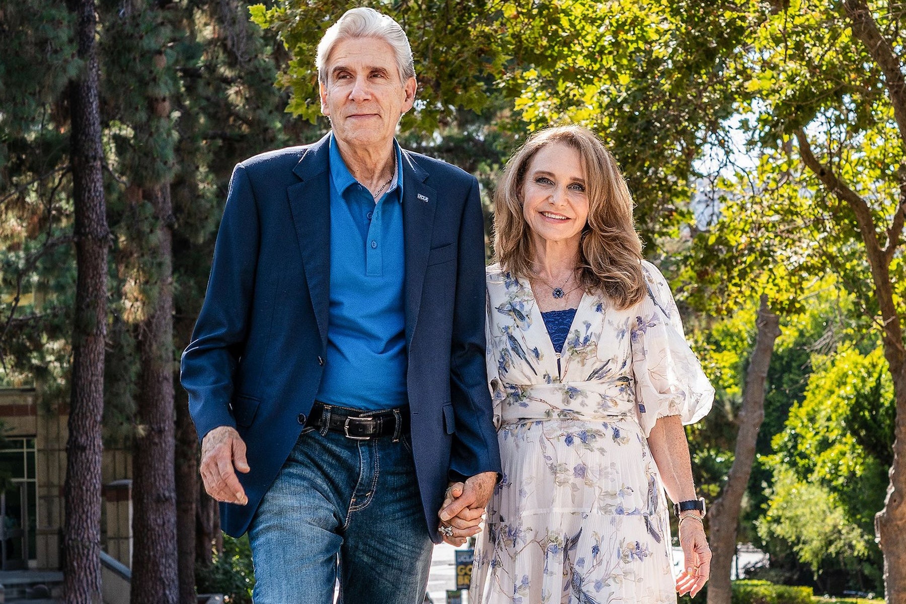 A couple stroll hand in hand along a sidewalk, enjoying a leisurely walk together and smiling at the camera