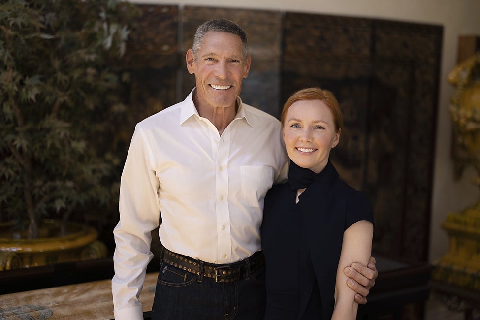 Photograph of a man and woman posing together, smiling in front of a plant