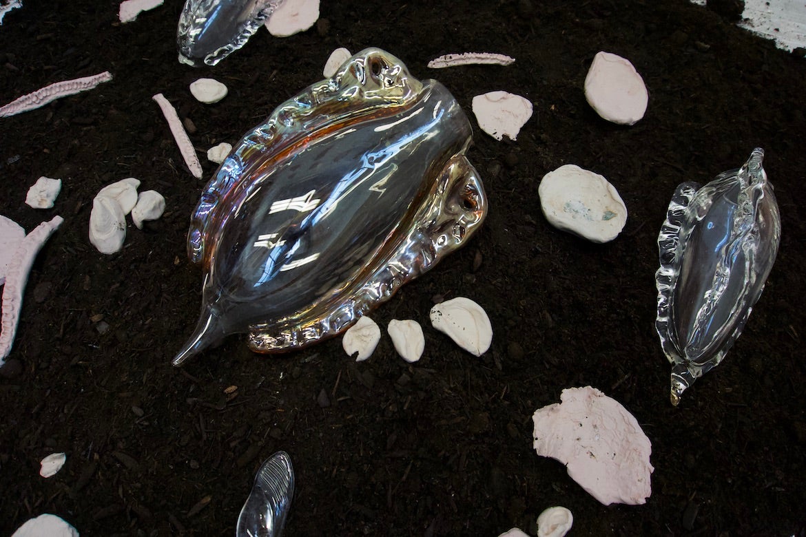 Modern, chrome, amorphous sculptures atop dark soil. 